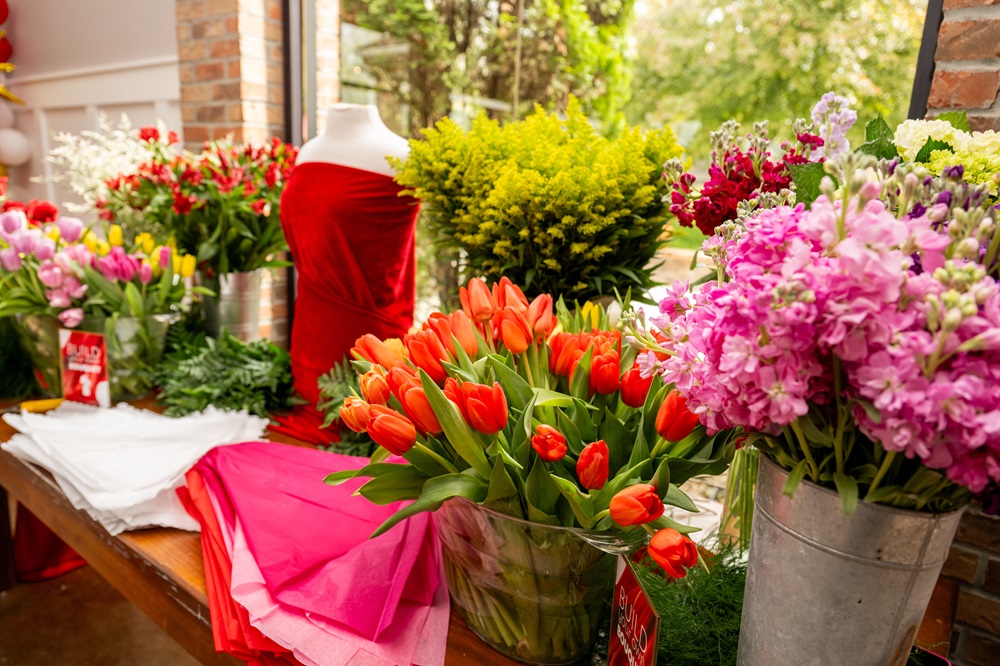 Dress form draped in red cloth surrounded by buckets of flowers.